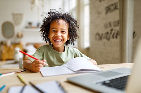 a child smiling while doing their homework at a table