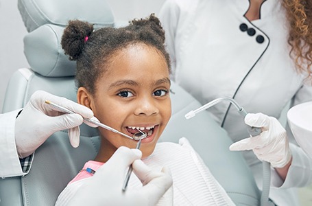 a child smiling and getting their teeth cleaned at the dentist’s office