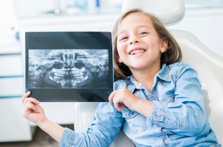 Child smiling and holding digital x-rays during tooth extraction process