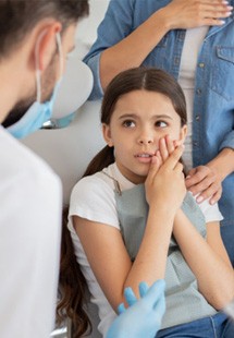 young girl with dental emergency looking at dentist 