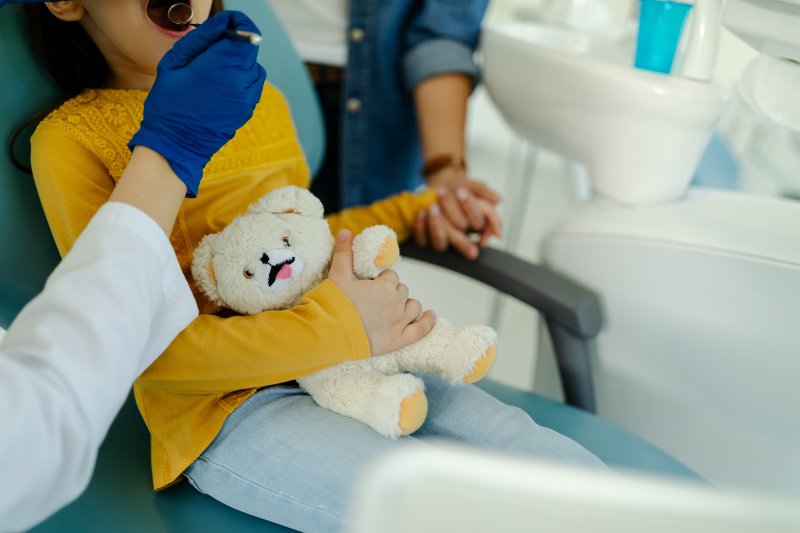 A child with dental anxiety holding a stuffed bear in the dentist's chair