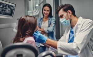 Dentist examines patient while mother looks on. 