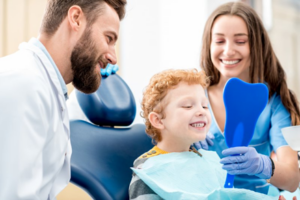 Child smiling while dentist and dental assistant hold a small mirror