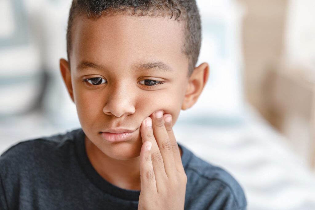 Little boy pressing fingers to cheek in pain